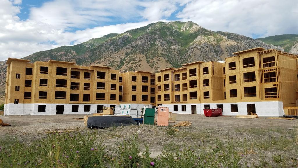 Wood framing in progress for a large multi-family residential building, set against a mountain backdrop.