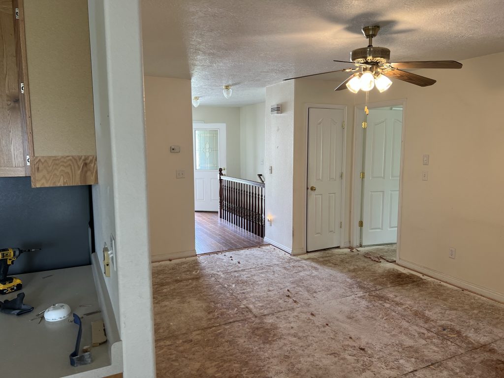 Living area with exposed subfloor, ceiling fan, and a view into the hallway and entryway.