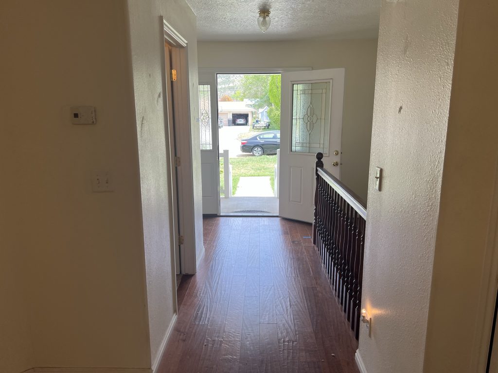 Bright entryway with hardwood flooring, glass-panel door, and a staircase railing leading to the hallway.