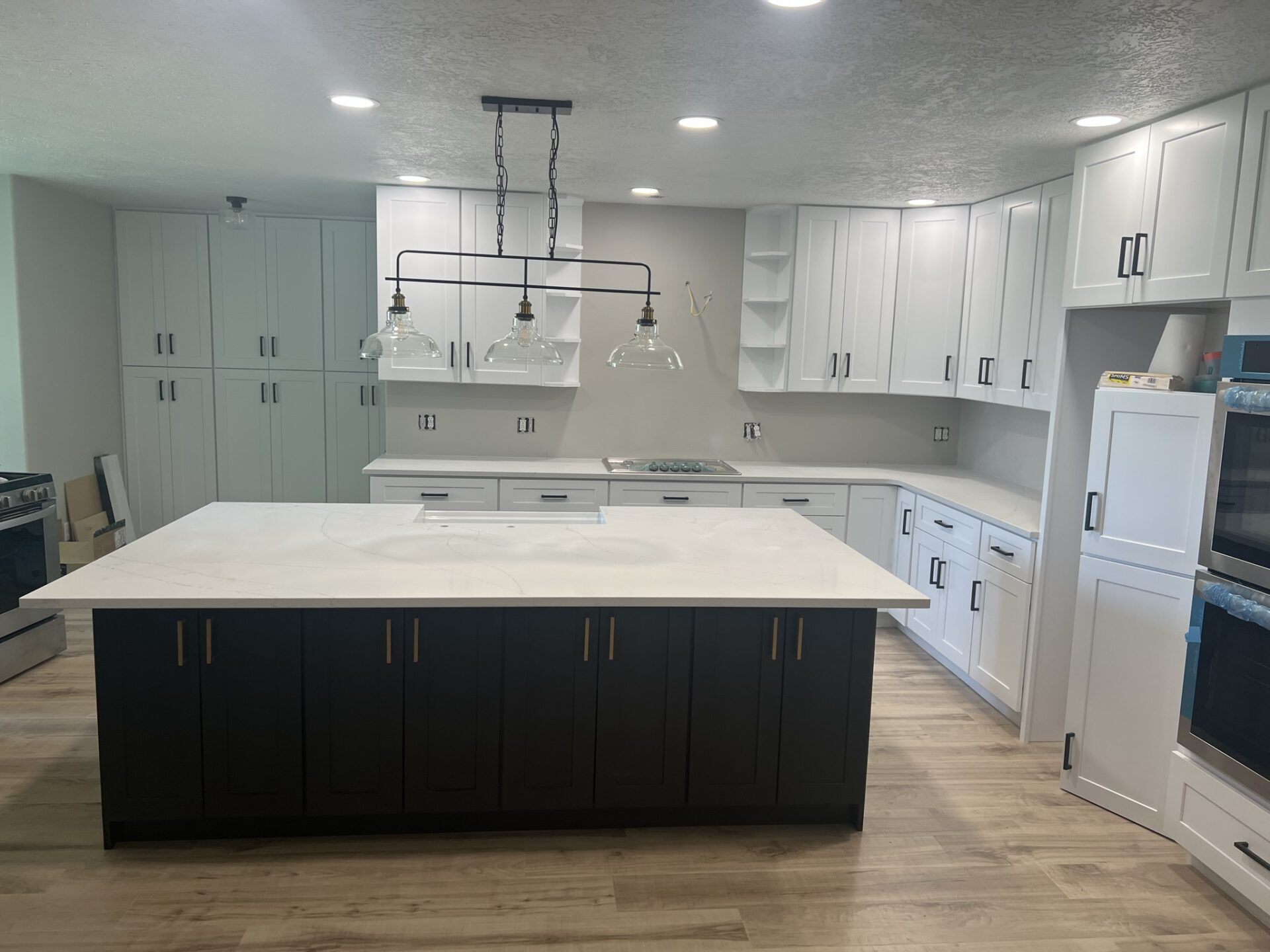 Spacious modern kitchen with white cabinetry, black island, quartz countertops, and a three-globe light fixture above.