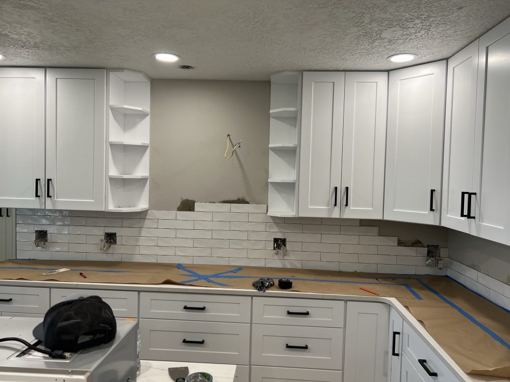 Kitchen remodeling in progress with white subway tile backsplash and white cabinets with black handles.