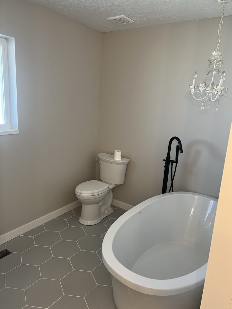 Bathtub and toilet installation in a minimalist bathroom remodel by Black Diamond Builders.