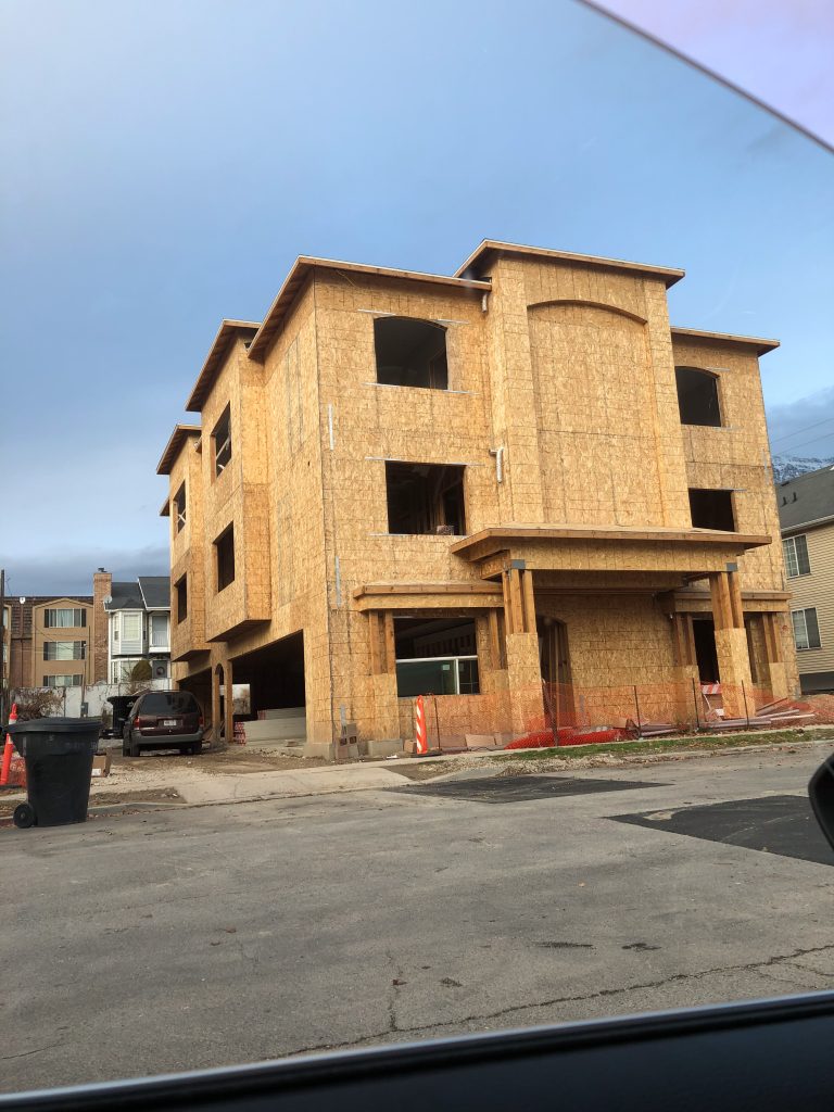 Wooden structure of a multi-family residential unit under construction, featuring large framed windows and a multi-story layout.