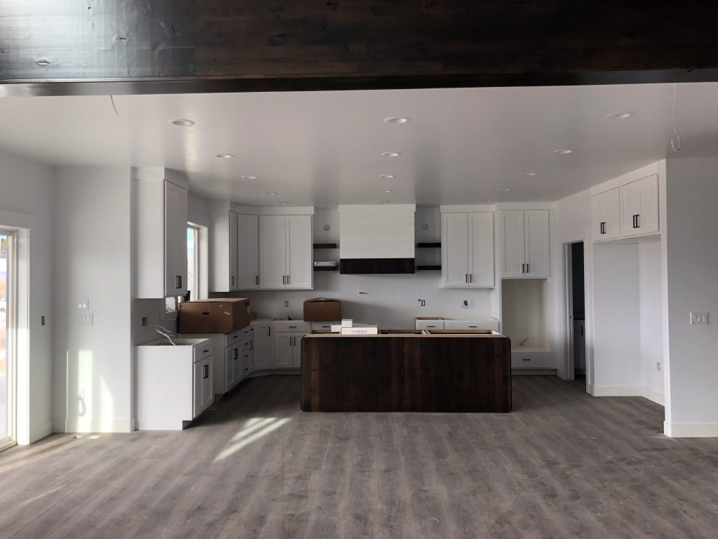Spacious open kitchen under construction with white cabinets, a dark wood island, and wood-look flooring.