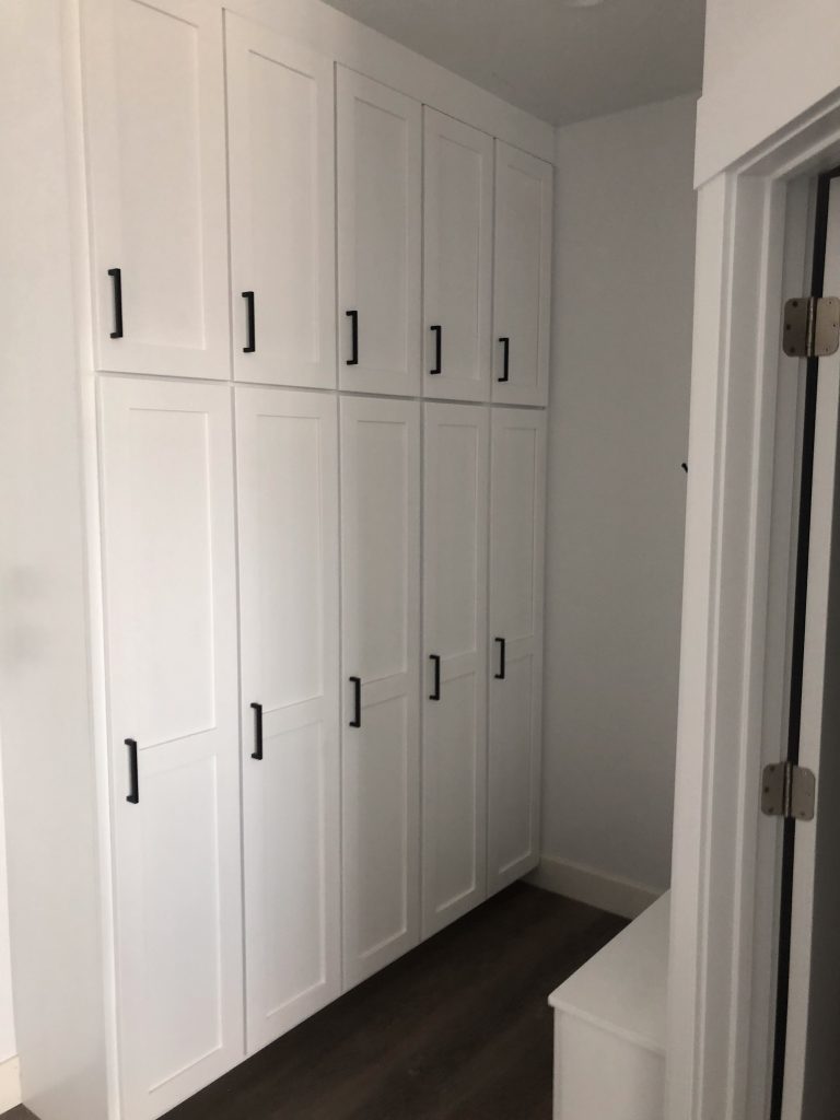 White built-in cabinets with black handles in a hallway or storage area.