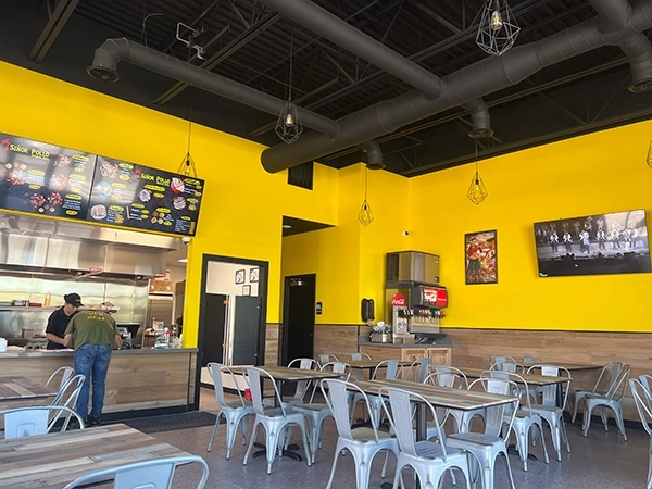 Restaurant interior with bright yellow walls, dining tables, menu boards above the counter, and a beverage station.