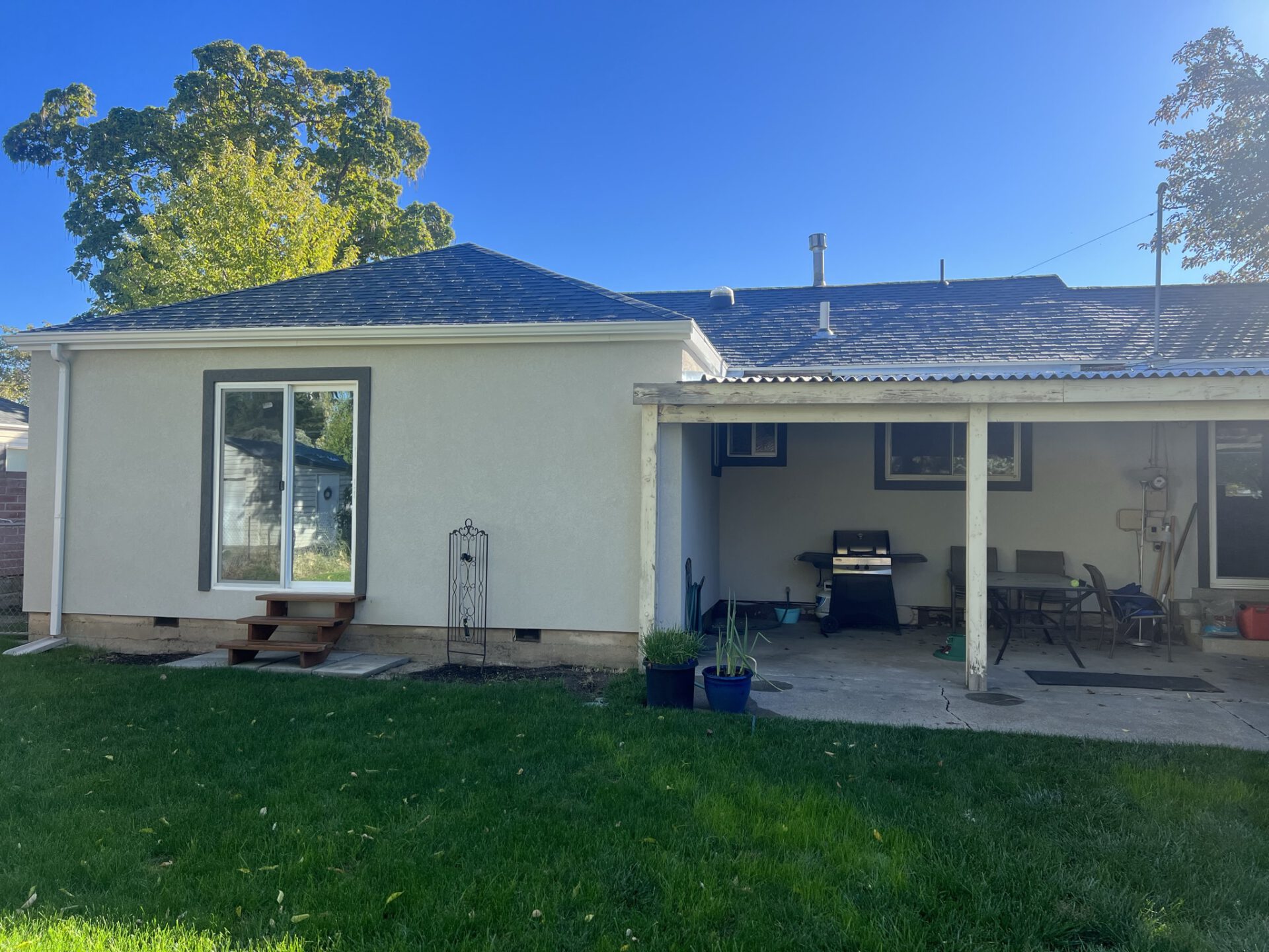 Backyard view of a house with a sliding glass door, covered patio, green lawn, and outdoor furniture.