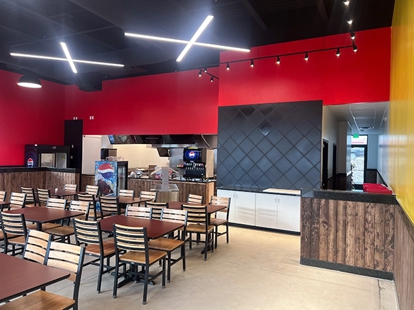 Modern restaurant interior with red and black walls, wooden dining tables, chairs, and a kitchen counter area.