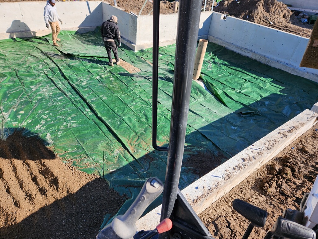 Workers preparing the foundation with a green protective cover for the guest house construction.